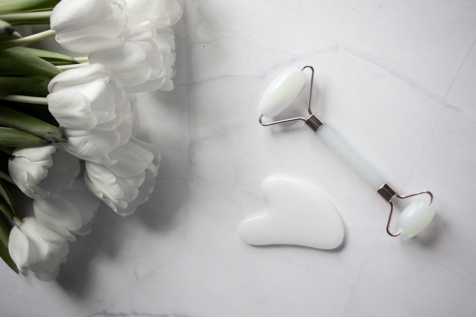 White Gua sha tools placed near bouquet of flowers on marble table
