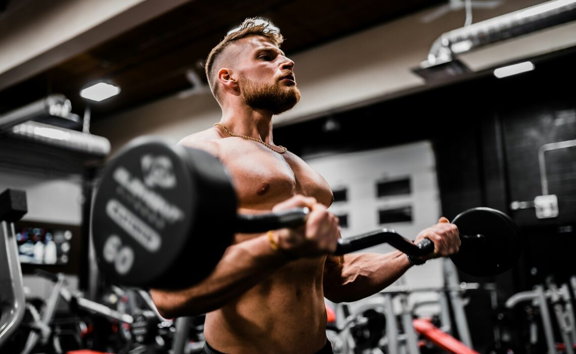 topless man in black shorts carrying black dumbbell