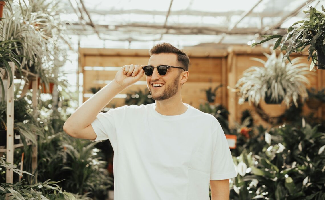 man in white crew-neck shirt wearing sunglasses standing near plants